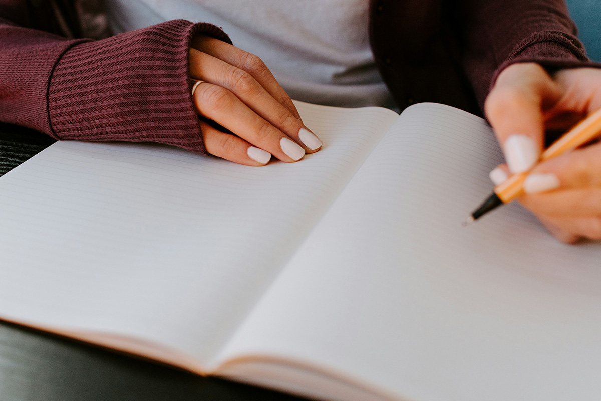 A woman writing on a blank notebook page with a stabilo pen.