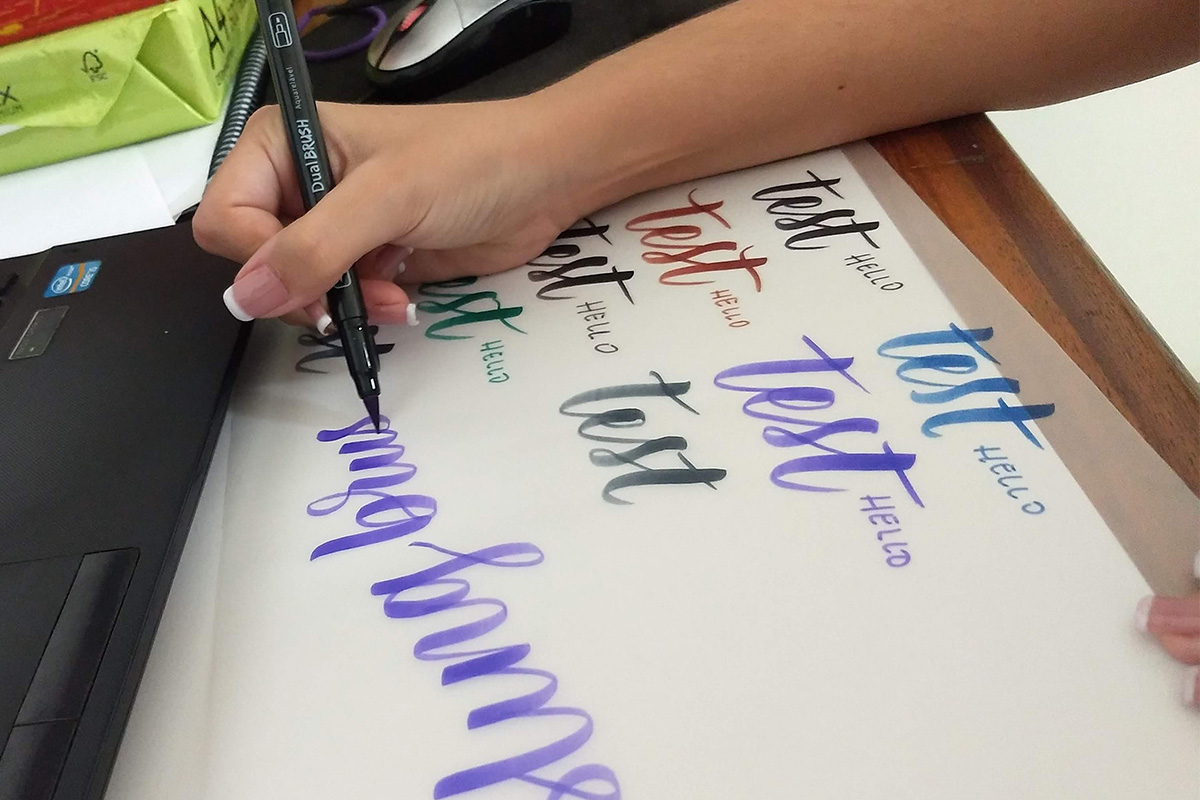 A woman's hand writing with a brush pen on a desk.